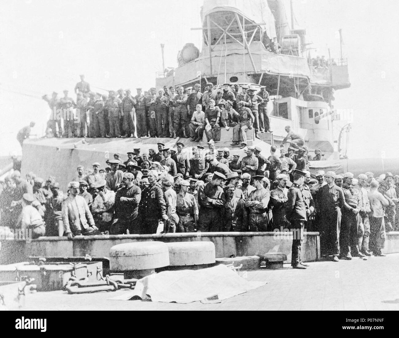 . Englisch: ein Gruppenfoto, einschließlich der deutschen Gefangenen, an Bord der HMS Inflexible (1907) ein Gruppenfoto aus dem vorschiff Der battlecruiser HMS Inflexible (1907) auf dem Weg zu einem Turm und die Brücke. Ein Türmchen hat bis Hafen ausgebildet worden. Eine große Gruppe von Matrosen in schmutzige Kleidung und Hüte stehen vor dem Turm mit einer anderen Gruppe auf dem Dach eines Revolvers. Die Gruppe soll deutschen Gefangenen, obwohl sie alle scheinen zu tragen alte schmutzige Kleidung und Caps, in der Regel, wenn das Schiff coaled getragen wird. Wenn Sie deutschen Gefangenen, dann ha Stockfoto