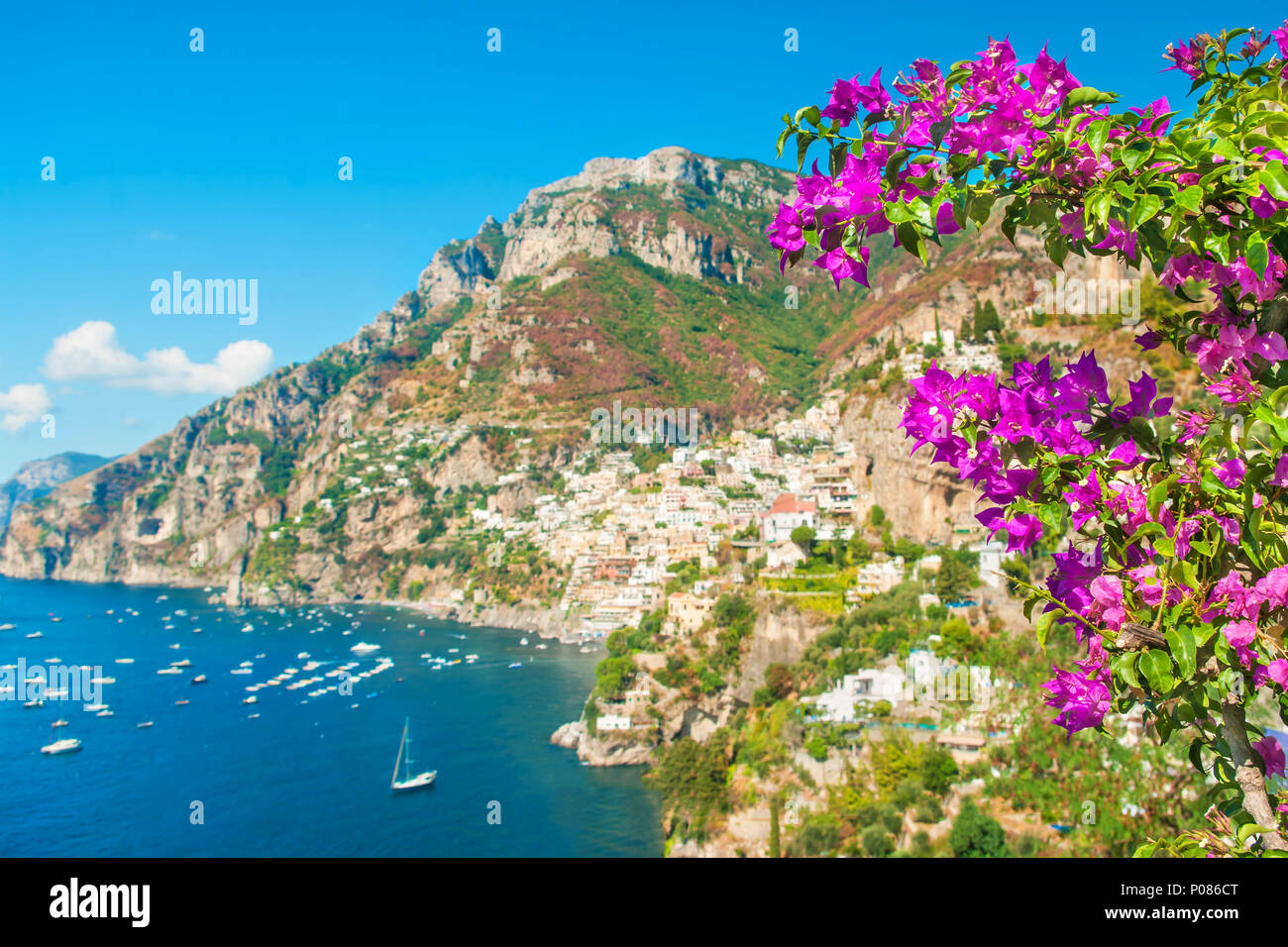 Defokussierten Blick auf kleine Küstenstadt auf der Bergseite mit lila Blüten im Vordergrund an sonnigen Sommertagen, Positano, Amalfi, Kampanien, Italien Stockfoto