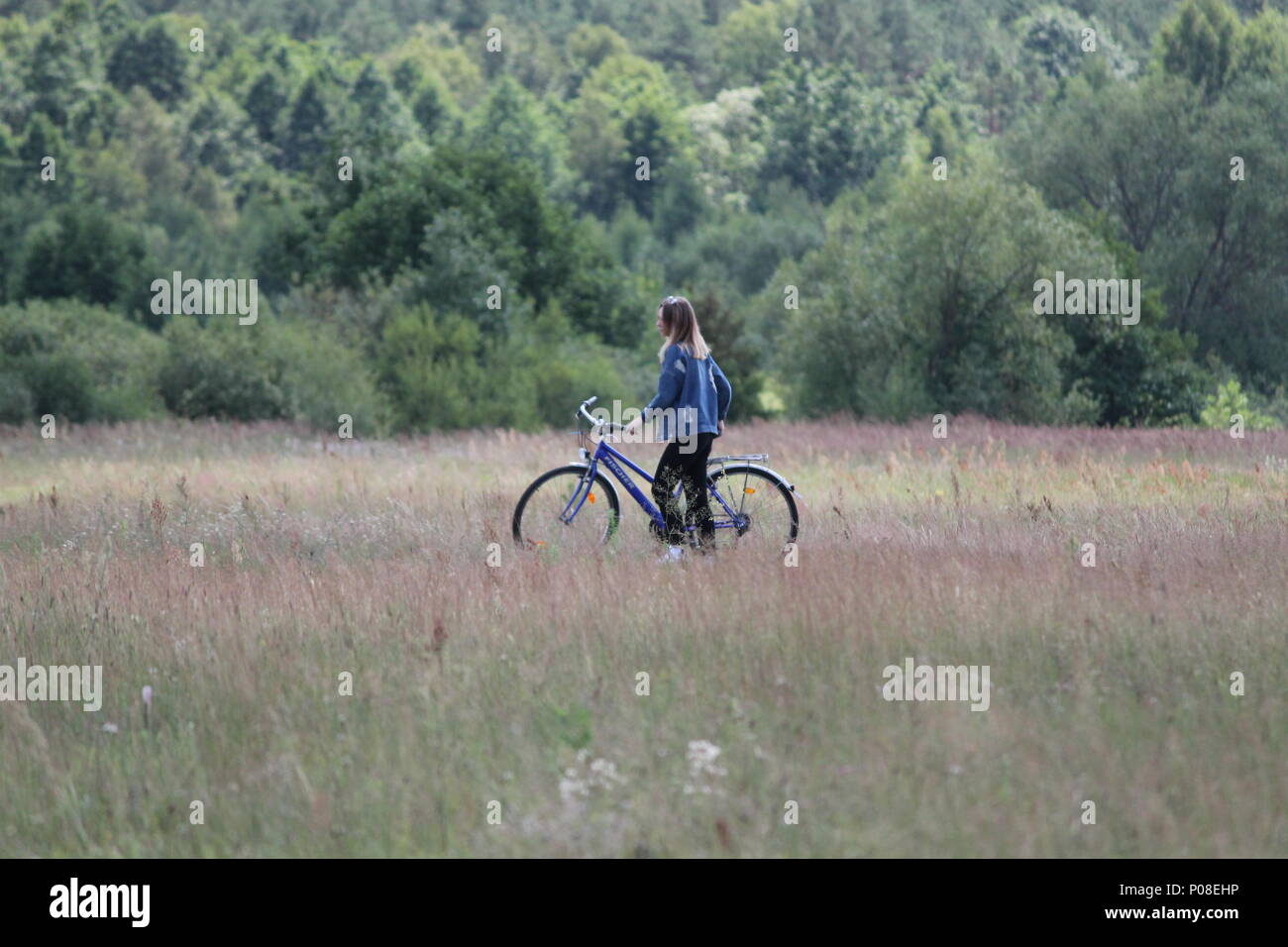 Schöne junge blonde Haare Frau Ritt auf dem Fahrrad auf frischen grünen Gras im Feld in warmen Frühlingstag Stockfoto