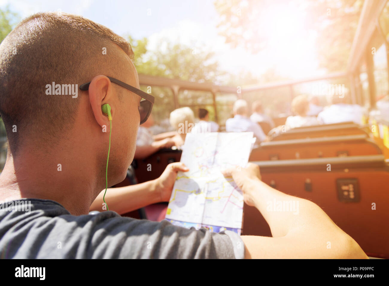 Nahaufnahme eines jungen cacausian Mann Reisen auf einem oben offenen tour bus, einen Stadtplan und das Tragen von Kopfhörern, mit einem Sonnenstrahl im Hintergrund Stockfoto