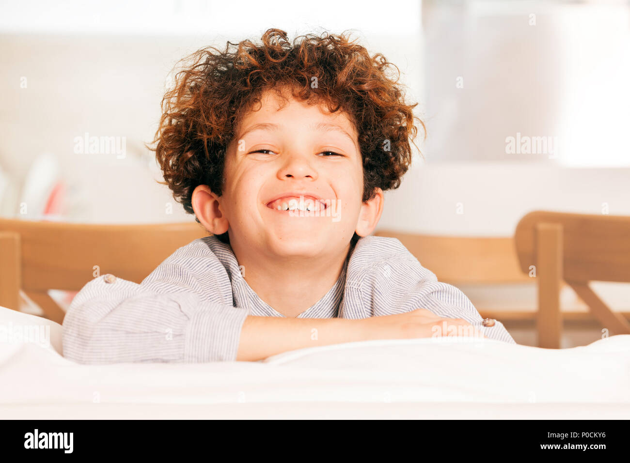 Portrait von niedlichen kleinen Jungen mit dem lockigen Haar auf dem Sofa sitzend, lachend und mit Blick auf die Kamera Stockfoto