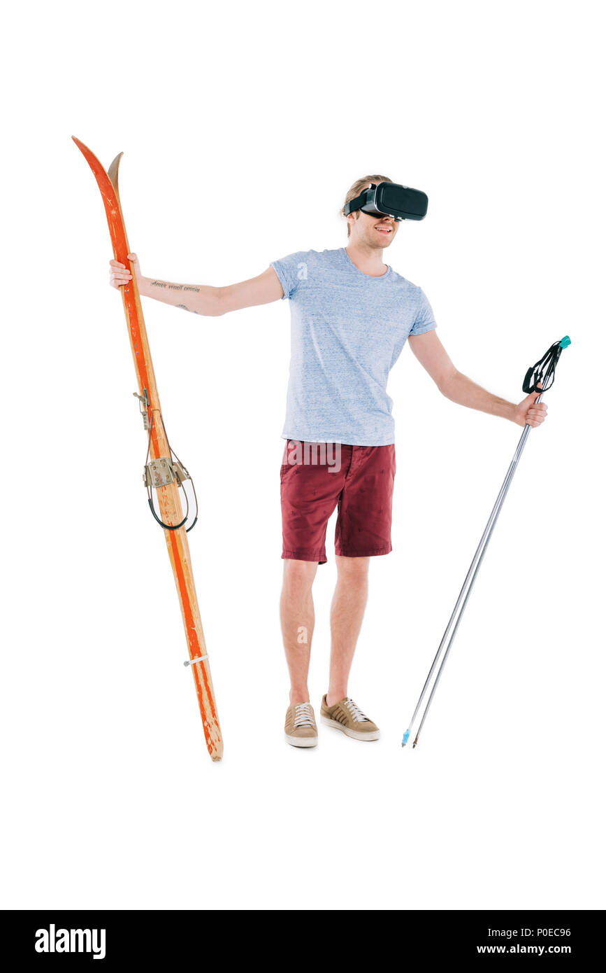 Hübscher junger Mann in virtual reality Headset holding Skier und Stöcke isoliert auf weißem Stockfoto