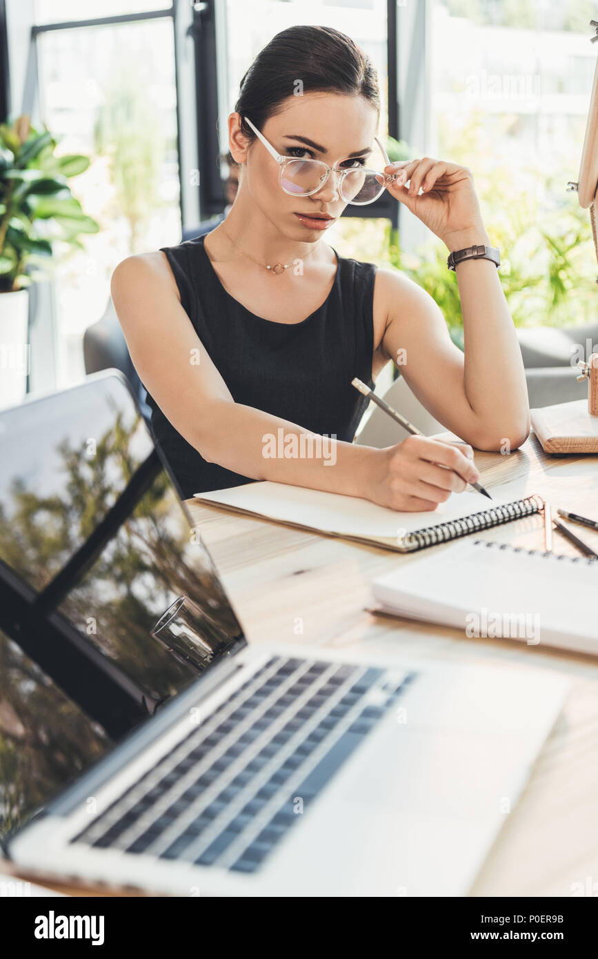 Junge schöne secretery am Schreibtisch im Büro schreiben in einem Notepad saßen und über ihre Brille Stockfoto