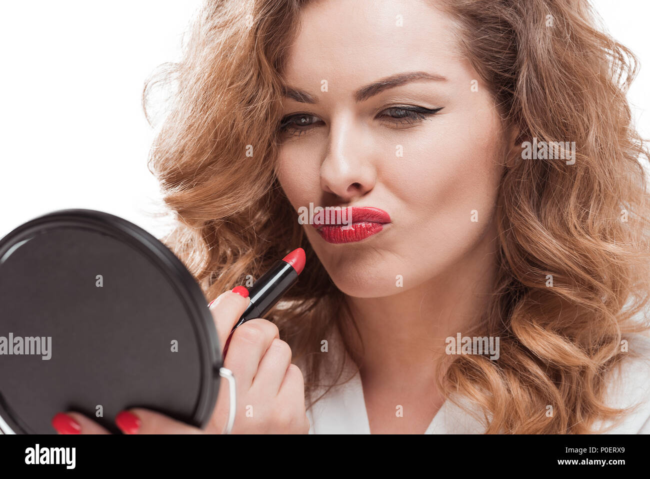 Grimasse Frau Anwendung Lippenstift in der Hand, während bei Spiegel isoliert auf weißem suchen Stockfoto