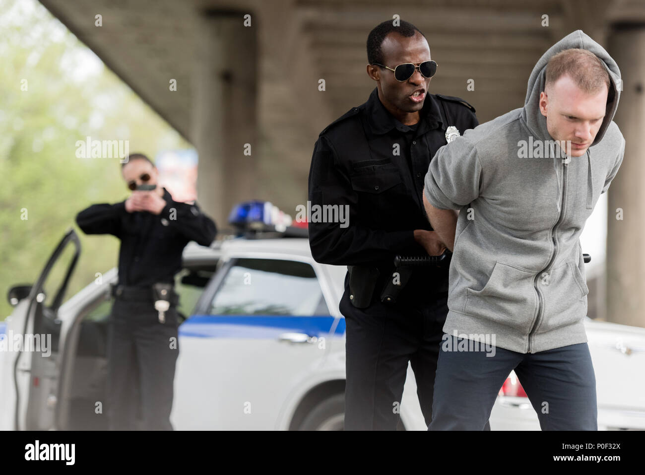 Wütend afrikanische amerikanische Polizisten verhaften junger Mann, während die weiblichen Partner ihn mit Pistole Stockfoto