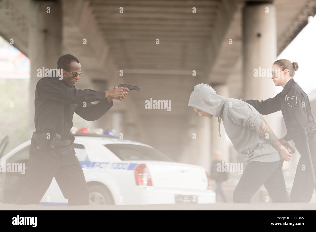 Seitenansicht der verärgerten Polizisten die Pistole auf die männliche Kriminelle, während ihn Partner Holding Stockfoto