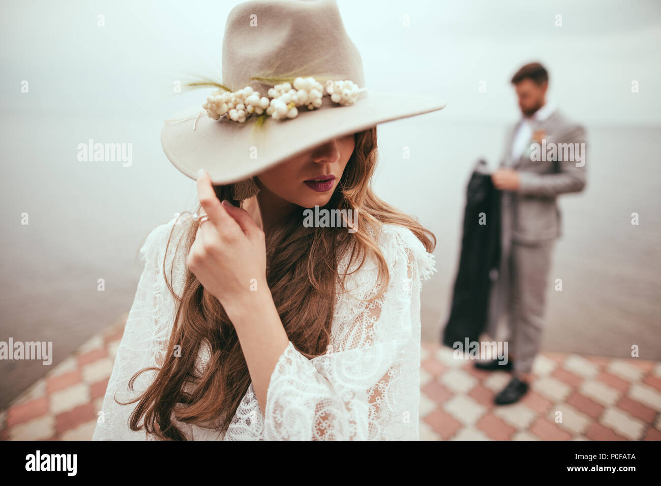 Schöne Braut Hochzeit Kleid und Hut in boho Style auf der Pier am See,  Bräutigam stehen hinter Stockfotografie - Alamy