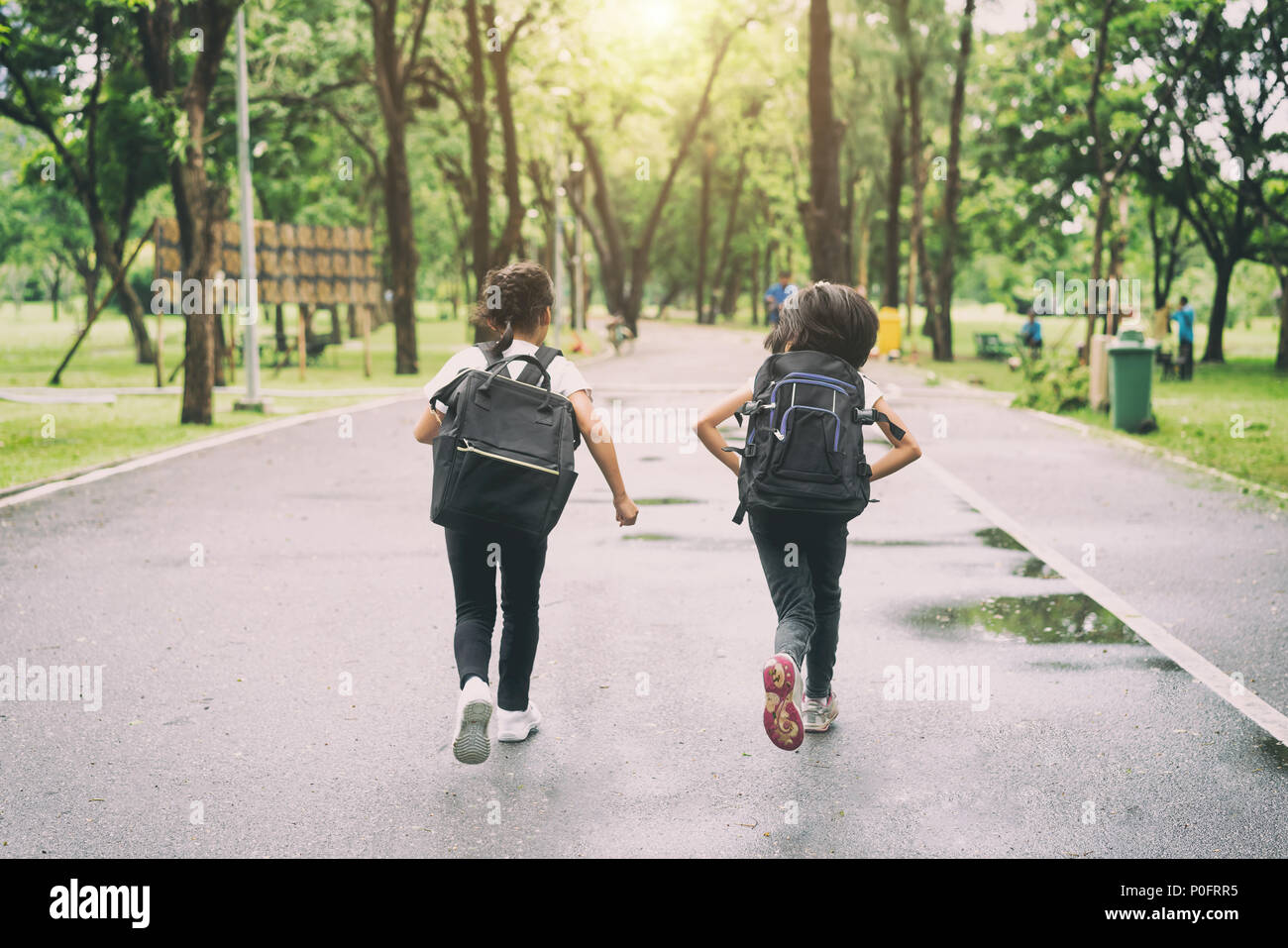 Zwei Schüler der Grundschule laufen Gehe zu Schule. Zwei Mädchen mit Taschen hinter dem Rücken. Warme Tag der Fall. Zurück zu Schule. Kleine Erstklässler. Stockfoto