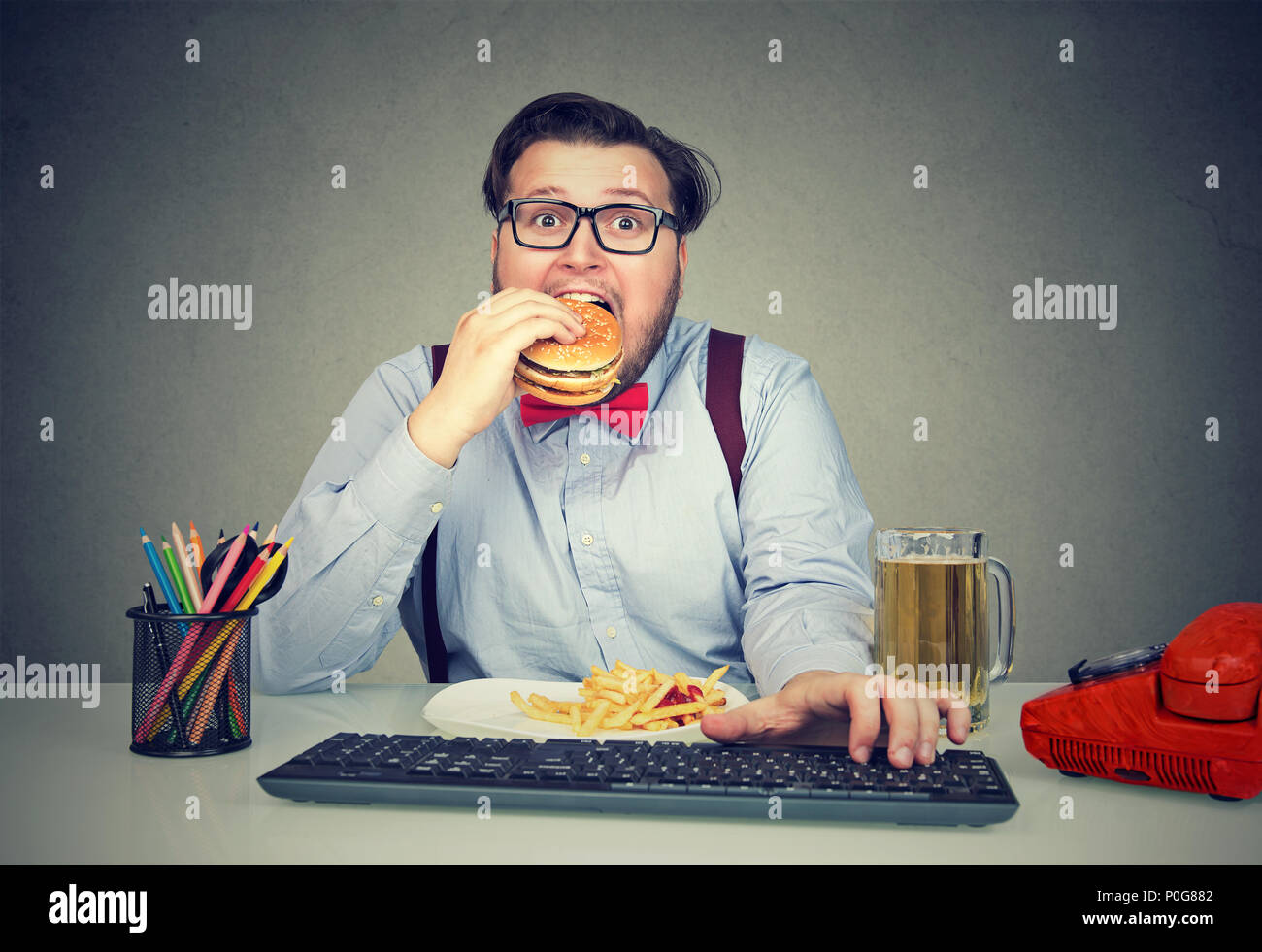 Übergewicht Geschäftsmann am Arbeitsplatz mit Computer und verbrauchen fast food Suchen super an † Kamera Hungrigen sitzen Stockfoto