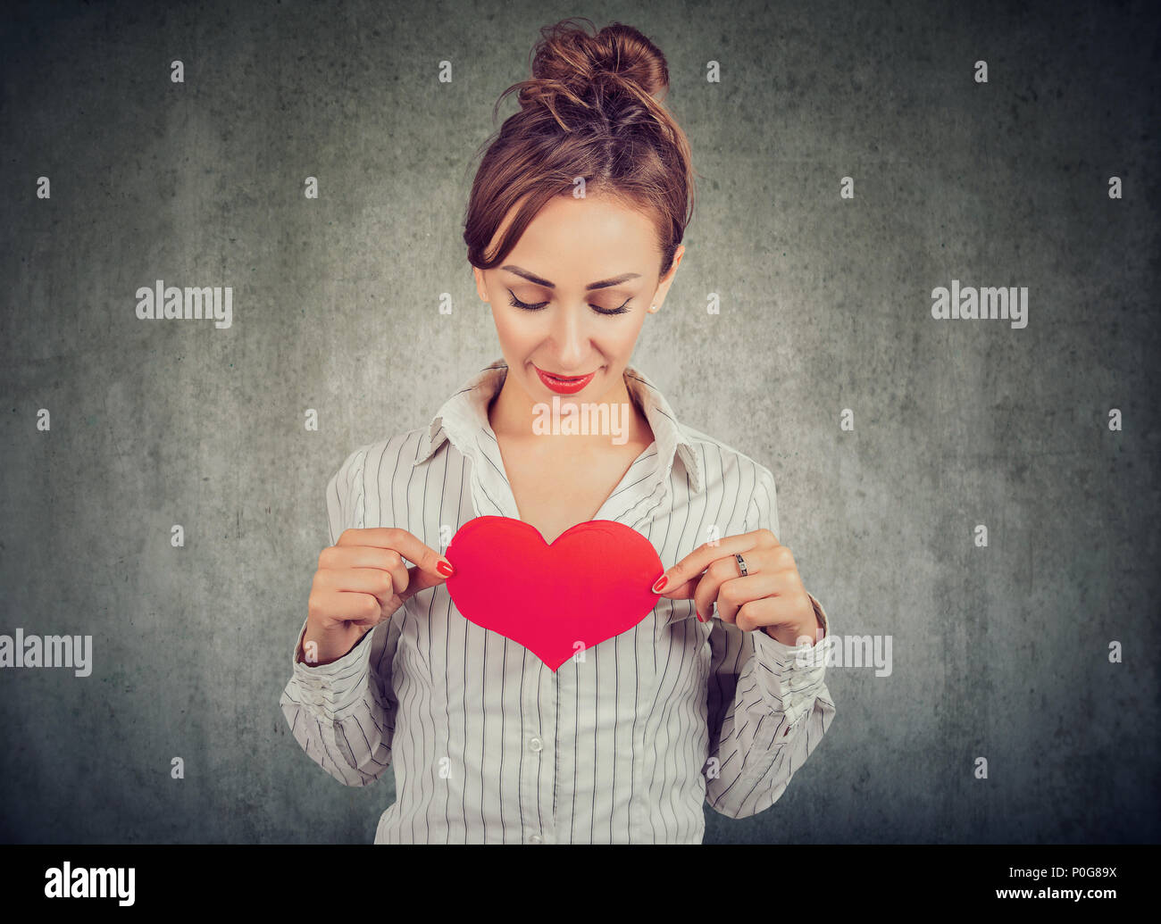 Hübsche Frau im Hemd Holding grosse rote Herz auf der Brust voll großer Gefühle auf grauem Hintergrund Stockfoto