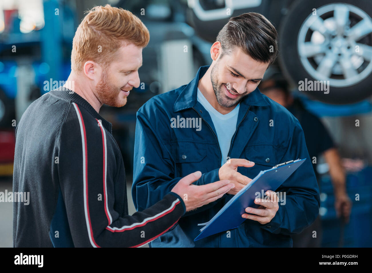 Junge automechanic angezeigt lächelnd Client eine Zwischenablage an eine Reparaturwerkstatt. Stockfoto