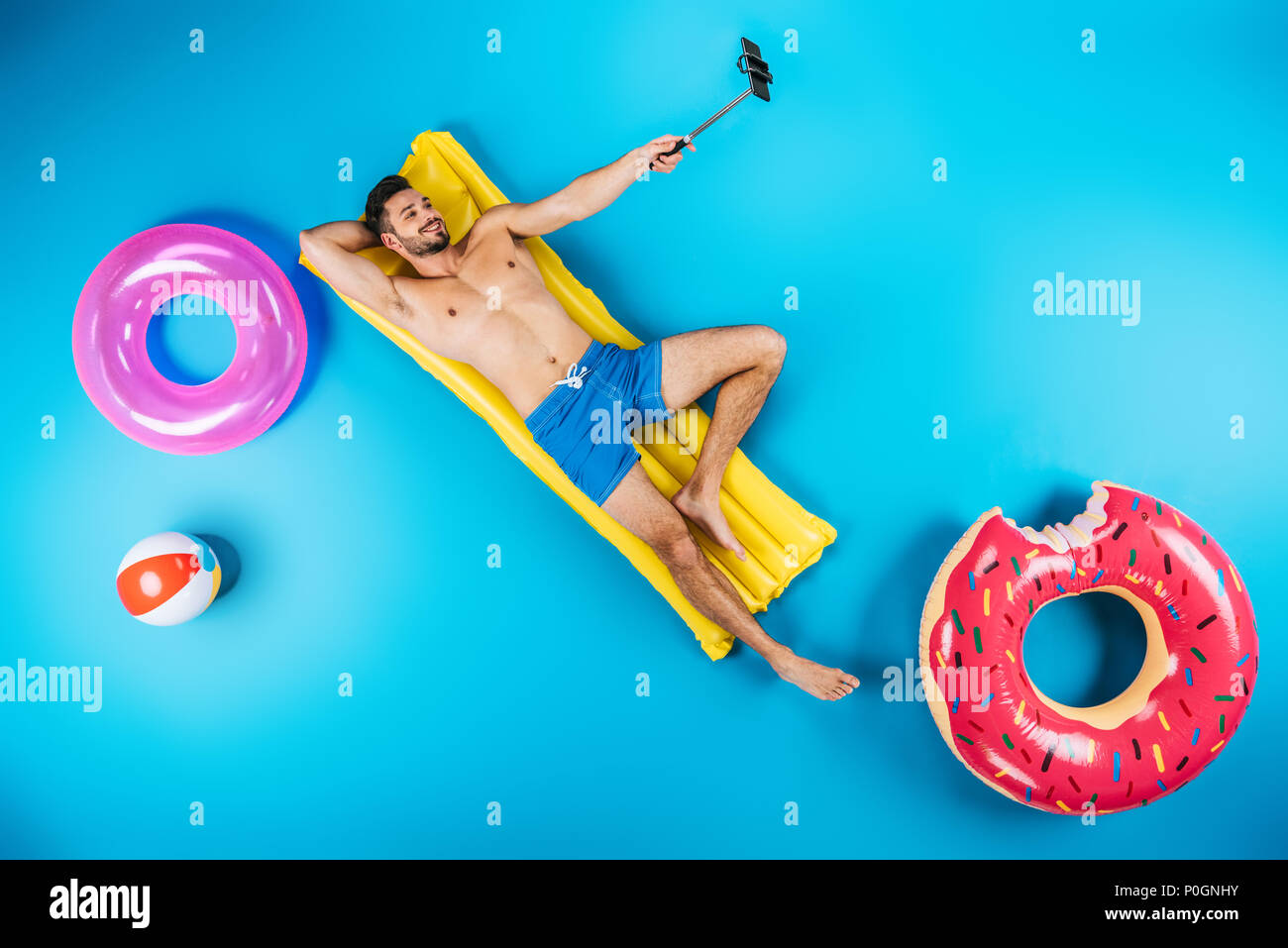 Blick von oben auf die Stattlichen lächelnden Mann ruht auf Schwimmen Matratze und unter selfie mit Smartphone auf Blau Stockfoto