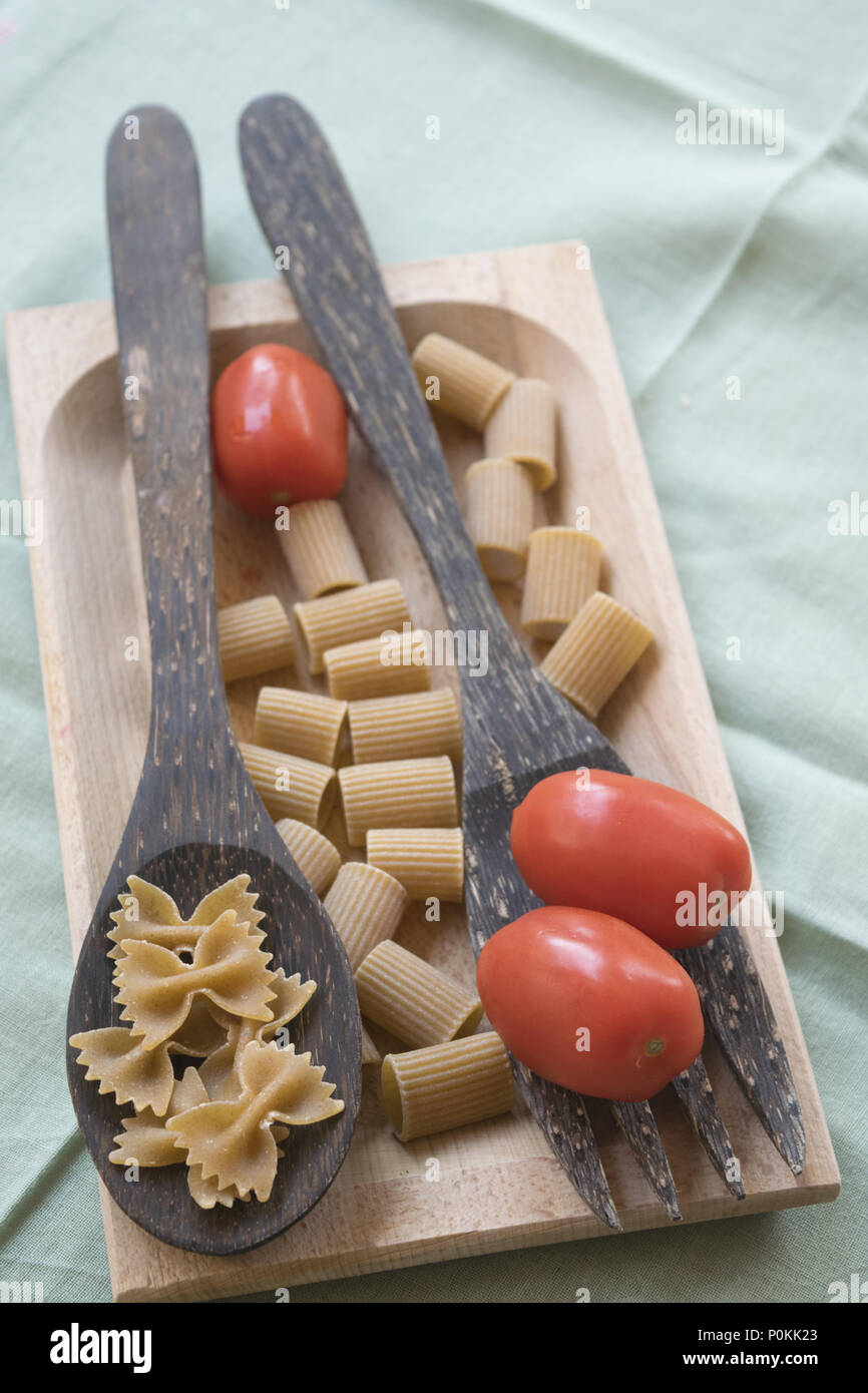 Vollkorn Schmetterling Pasta auf einer hölzernen Schöpfkelle und frische Kirschtomaten Stockfoto