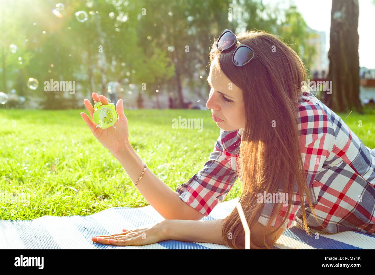 Junge Frau mit Wecker in Ihrer Hand. Hintergrund sunny City Park, kopieren Raum Stockfoto