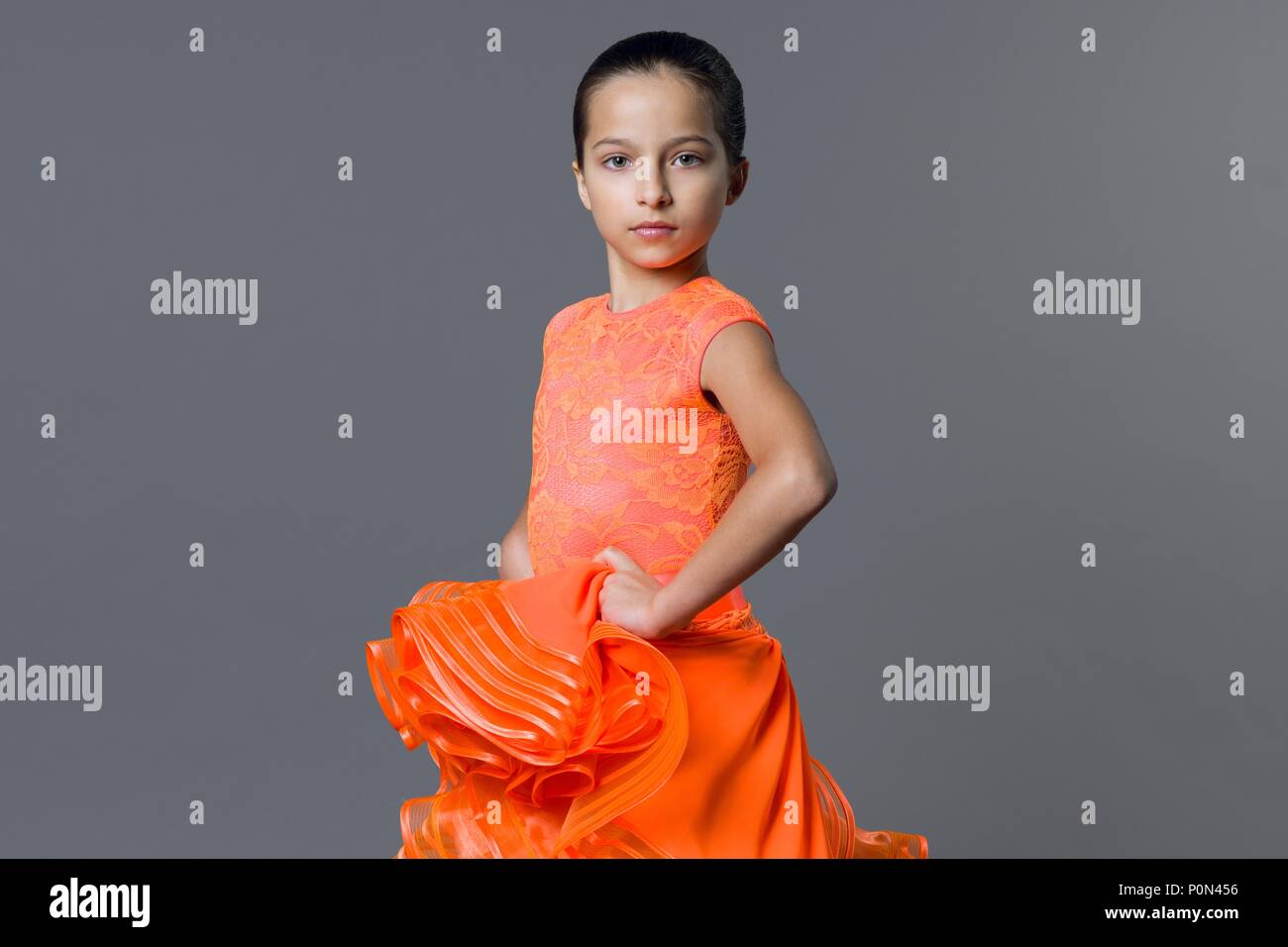 Porträt eines Mädchens, das Kind 9-10 Jahre Tänzer. Sport Gesellschaftstänze, Latino. Mädchen in einem orangefarbenen Kleid auf einem grauen studio Hintergrund Stockfoto