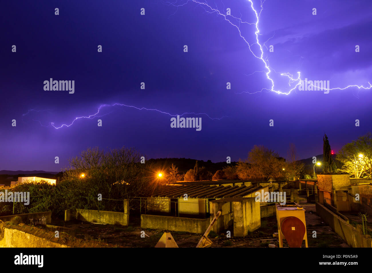 Helle Blitze rissen auf Violett Abendhimmel während Gewitter über die Häuser der kleinen Stadt Stockfoto