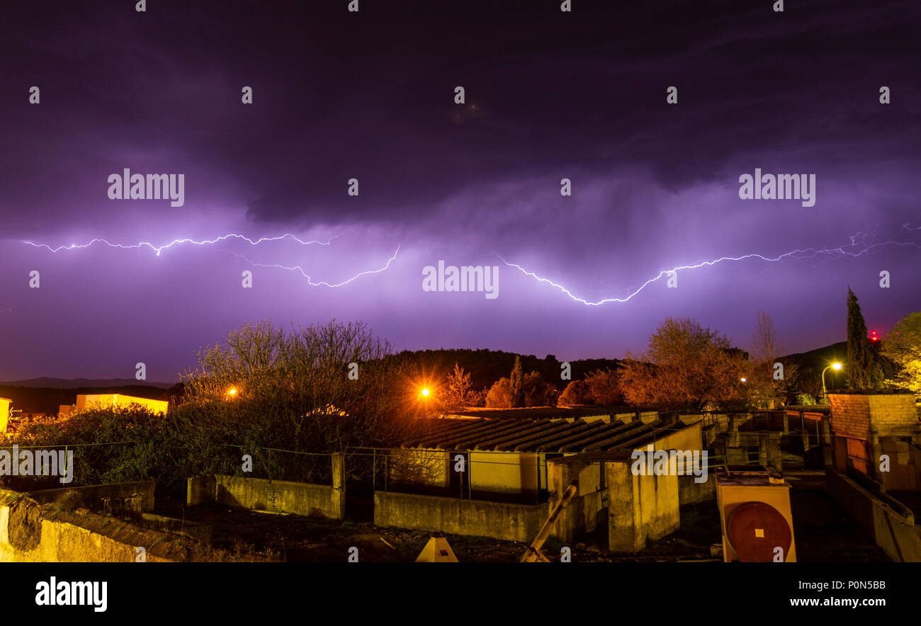 Helle Blitze rissen auf Violett Abendhimmel während Gewitter über die Häuser der kleinen Stadt Stockfoto