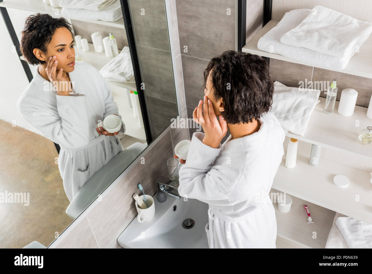 Afrikanische amerikanische Frau Auftragen kosmetischer Anti-Falten-Creme im Gesicht und in den Spiegel im Bad Stockfoto