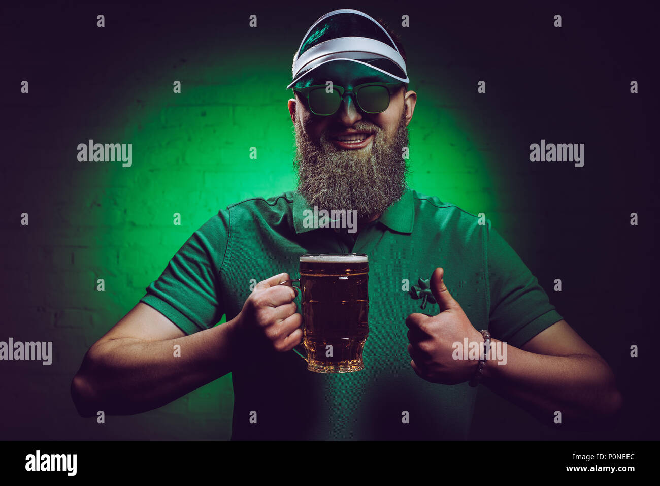Lächelnd bärtigen Mann hält ein Glas Bier und zeigen Daumen hoch, st patricks day Konzept Stockfoto
