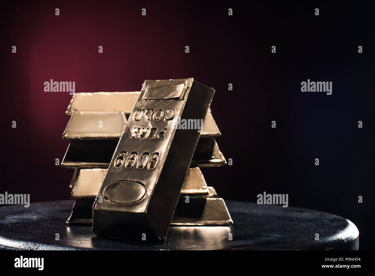 Stapel von goldenen Barren auf Tisch vor rotem Hintergrund Stockfoto