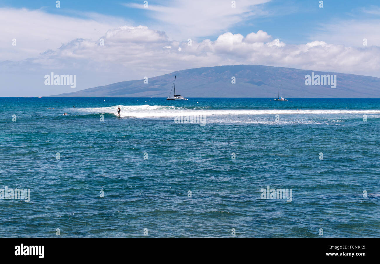 Surfer fangen eine kleine Welle vor Maui mit der Insel Lana'i im Hintergrund. Stockfoto