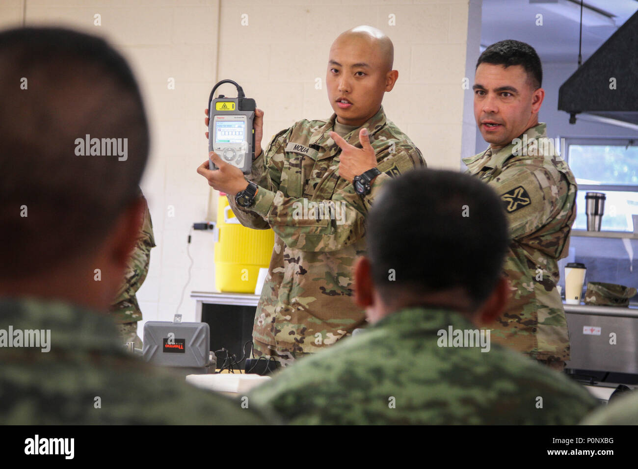 Armee finden Spc. Yee Moua (links), einen chemischen, biologischen, radiologischen und nuklearen (CBRN) Specialist und heimisch in Appleton, Wisconsin, an die 388 Unternehmen der Chemischen Industrie zugeordnet, 472Nd chemische Bataillon, 76 Operationelle Antwort Befehl, erklärt die Funktionalität einer chemischen Detektors zu einer Gruppe von fast 30 mexikanische Armee Soldaten, während Sgt. Jose Lugo, Sprachwissenschaftler und heimisch in Bremerton, Washington, zu der 341 Military Intelligence Battalion zugeordnet, übersetzt während eines CBRN-Klasse im Camp Äsche, Michigan 6. Juni als Teil der Übung Fuerzas Amigas. Die mexikanische Armee Soldaten haben t ausgegeben Stockfoto
