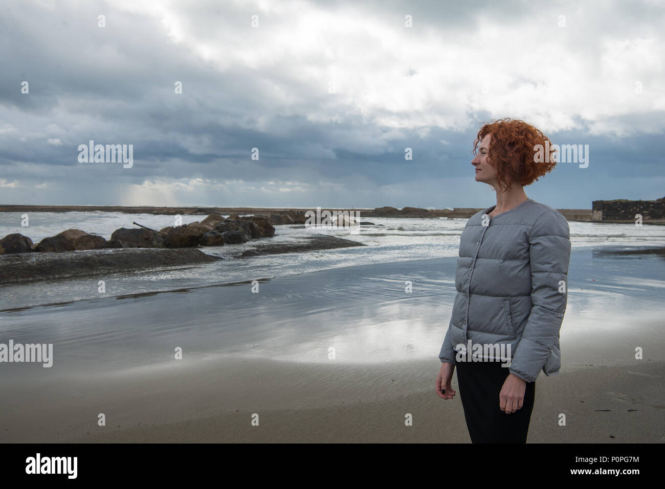 Glückliche junge Frau in Puffer jacke Seashore an bewölkten Tag, Anzio, Italien Stockfoto