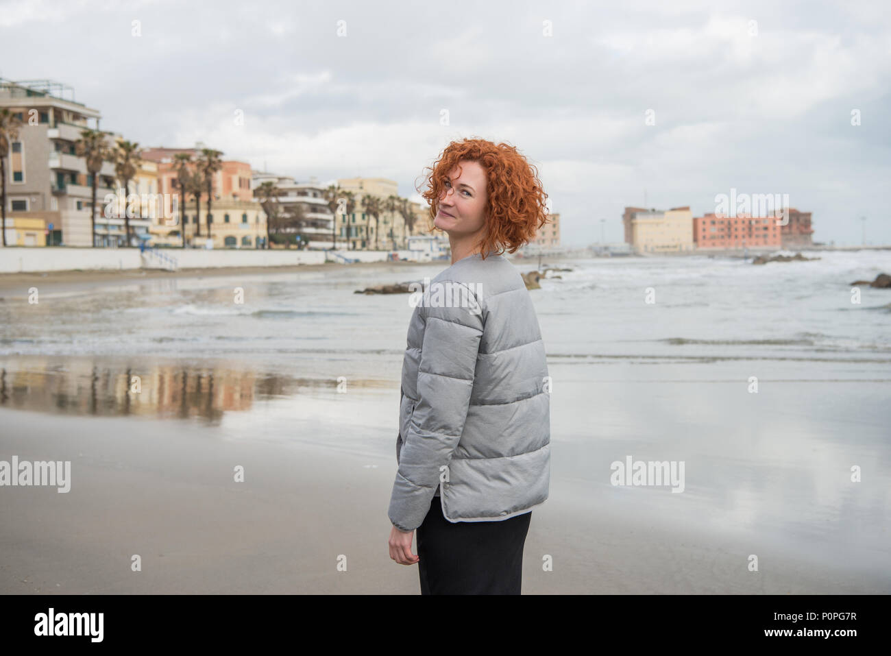 Glückliche junge Frau in Puffer Jacke am Meeresufer, Anzio, Italien Stockfoto