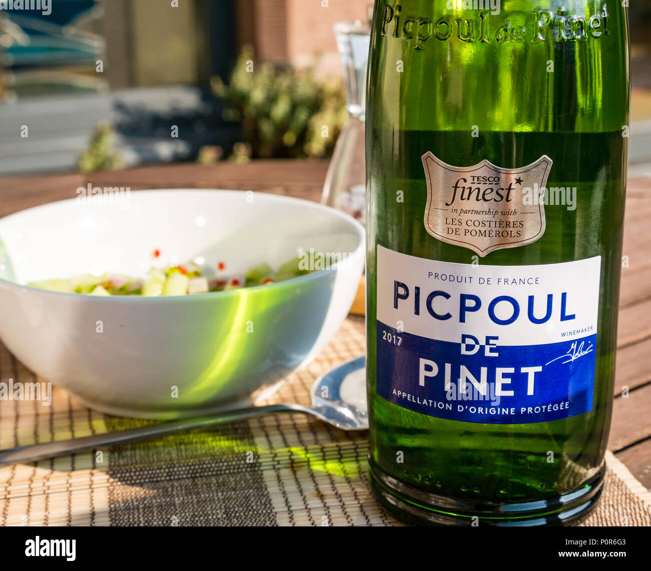 In der Nähe des Tesco Finest Picpoul de Pinet grüne Flasche Wein auf der Terrasse im Sonnenschein mit Schüssel Gurkensalat Stockfoto