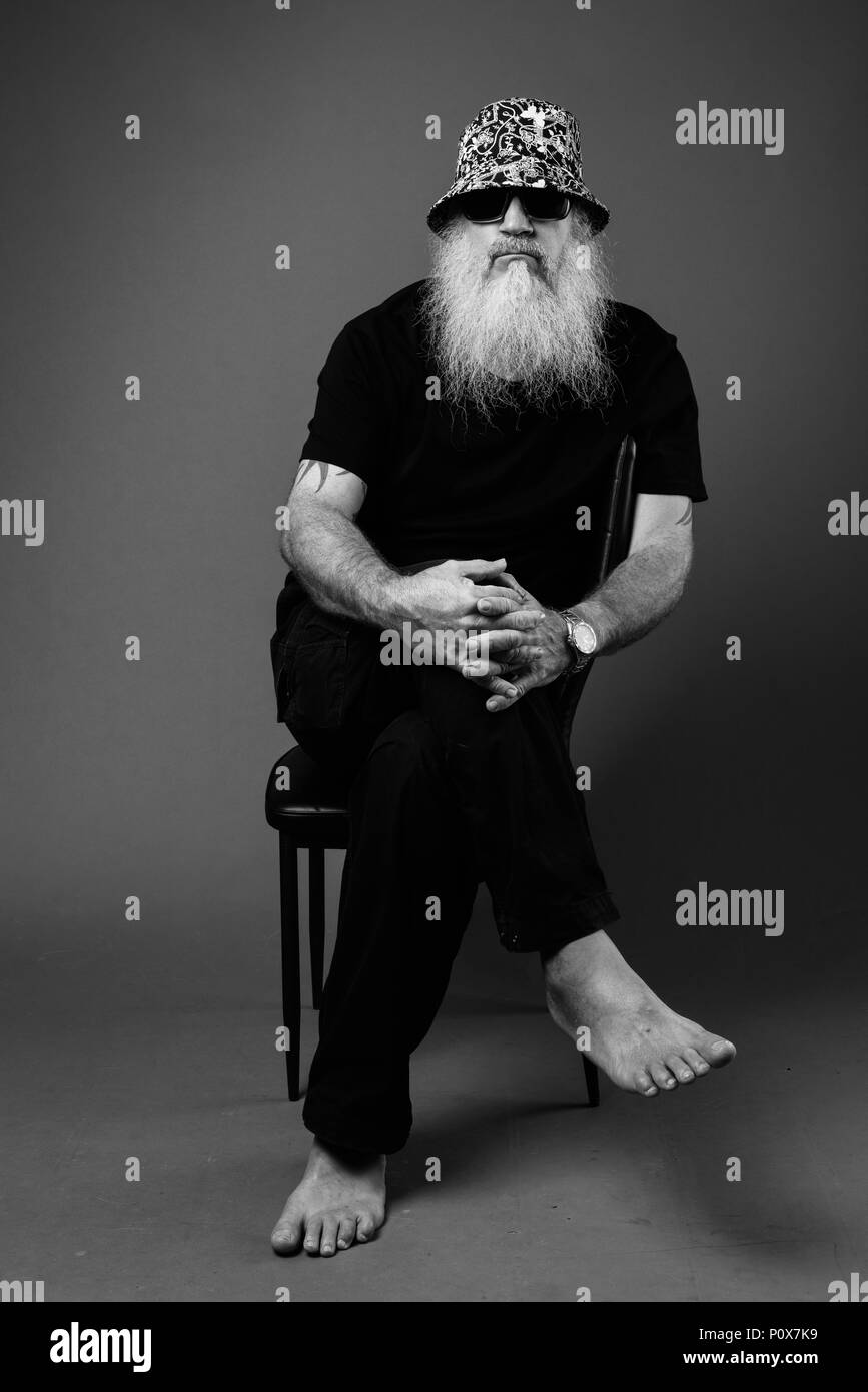 Schwarz-weiß-Porträt zur Reife der glatzköpfige Mann mit langem Bart sitzt Stockfoto
