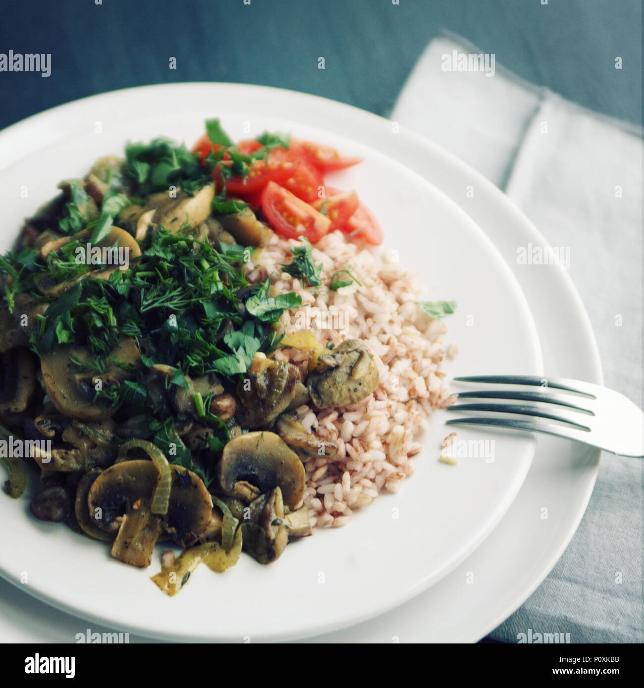 Roter Reis mit Pilzen und Tomaten. Vegane Gerichte. Europäische Küche. Einfach gesundes Mittagessen. Vegetarisches Reisgericht auf dem weißen Teller. Close Up. Zu Stockfoto