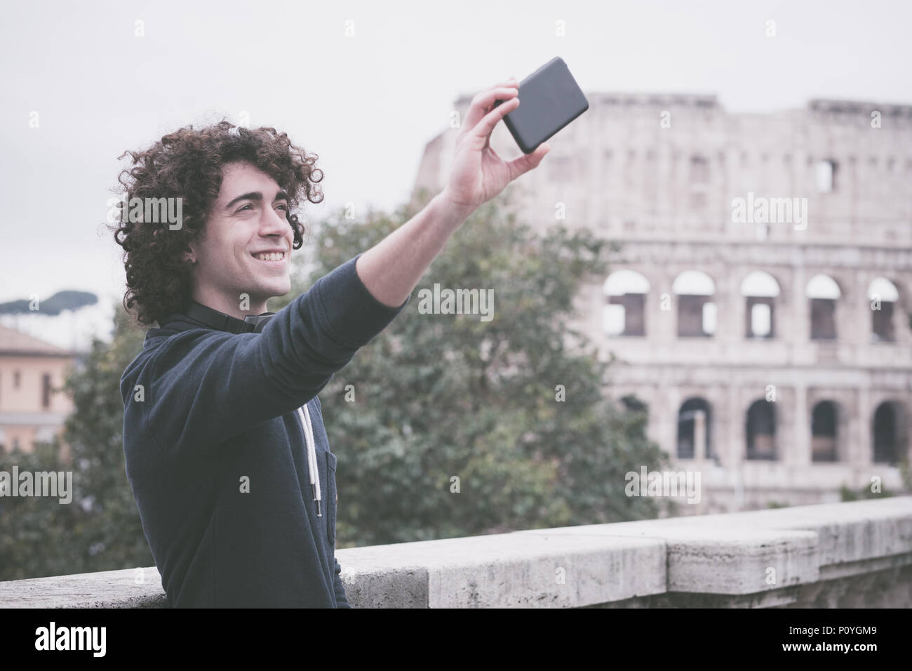 Hübscher junger Mann mit lockigem Haar lächelnd und unter selfie mit seinem Handy Stockfoto