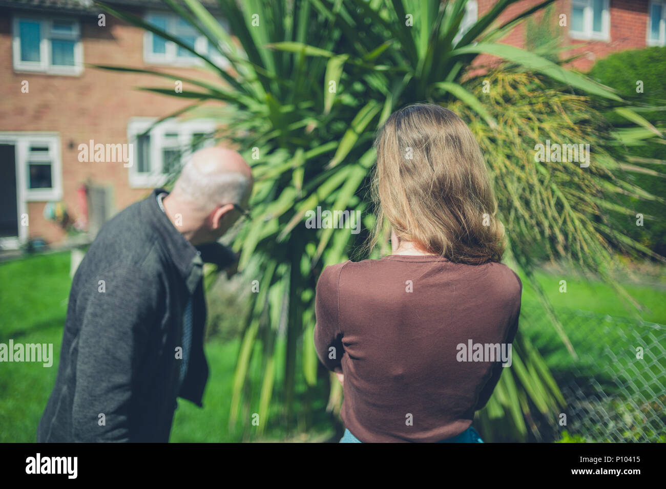 Ein älterer Mann und junge Frau in einem Garten auf einer Palme zeigen Stockfoto
