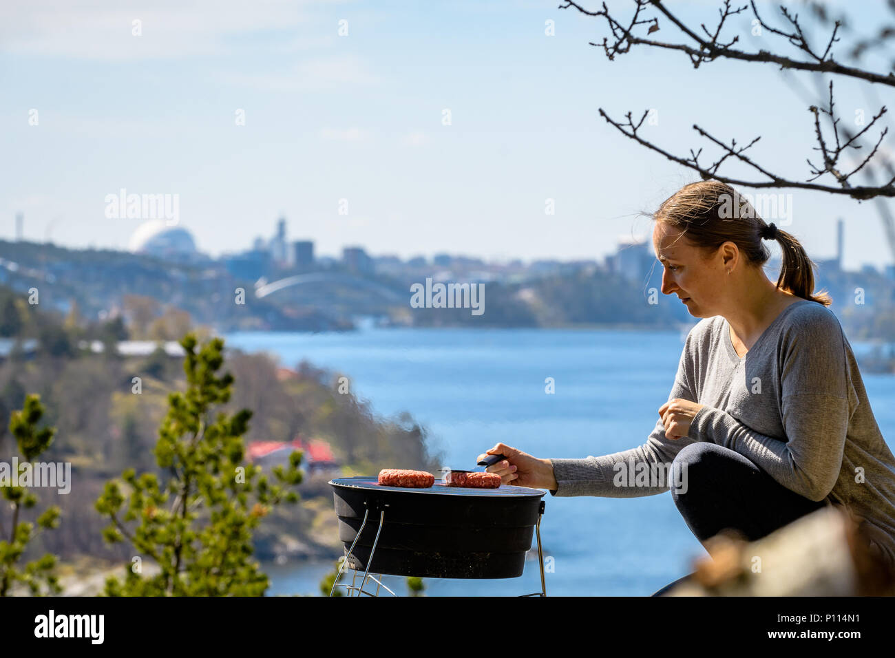 Frau Hamburger Grillen im Freien vor der Stockholmer Skyline Stockfoto