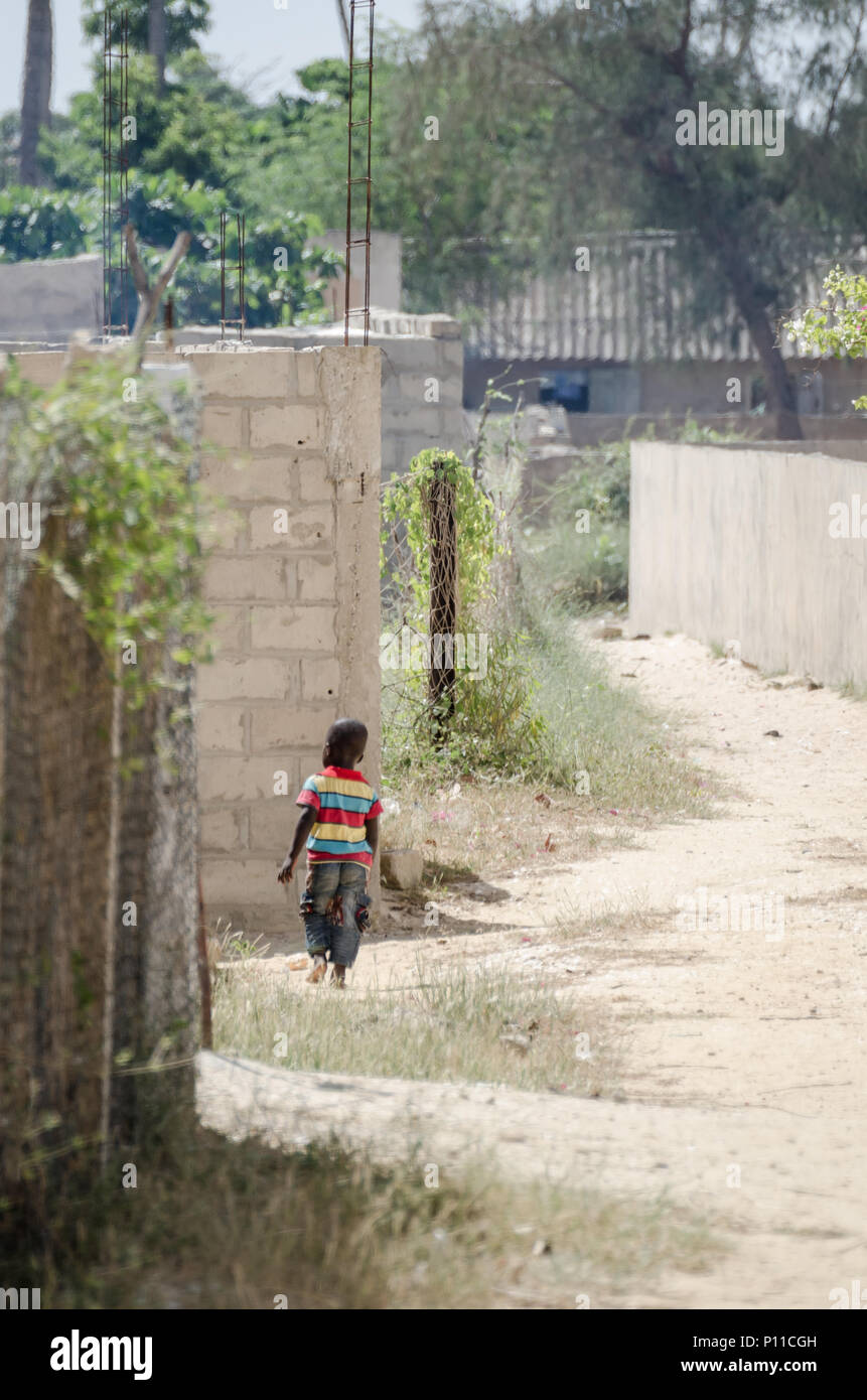 Saint-Louis, Senegal - Oktober 20, 2013: Nicht identifizierte Junge afrikanische Junge mit bunten Shirt zu Fuß durch sandige Straße Stockfoto