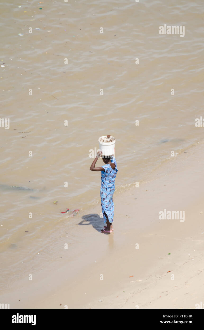 Nicht identifizierte afrikanische Frau im blauen Kleid am Strand balancing Schaufel Stockfoto