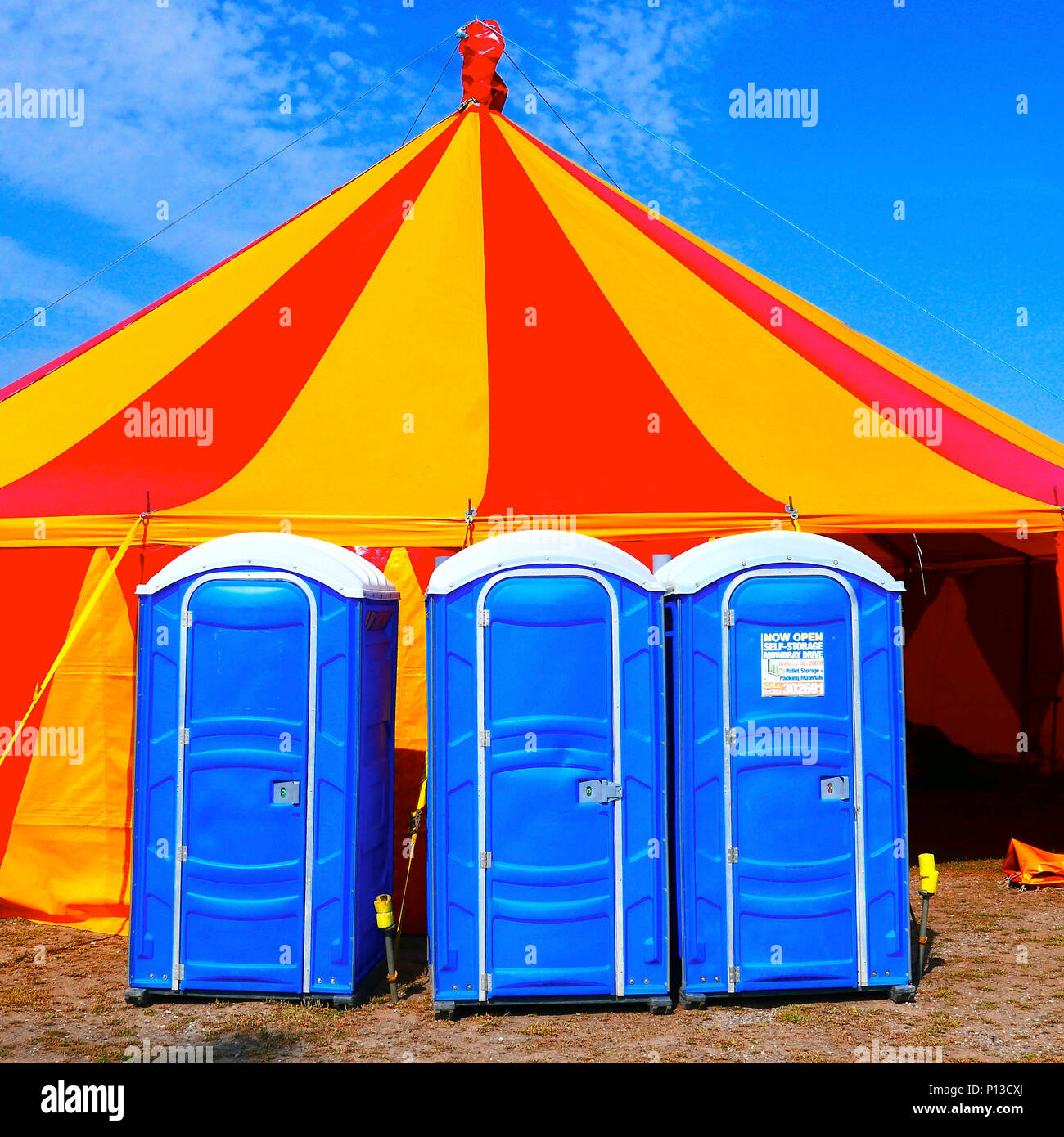 Rote und gelbe Festzelt gegen den blauen Himmel mit blauen mobile Toiletten an der Vorderseite Stockfoto