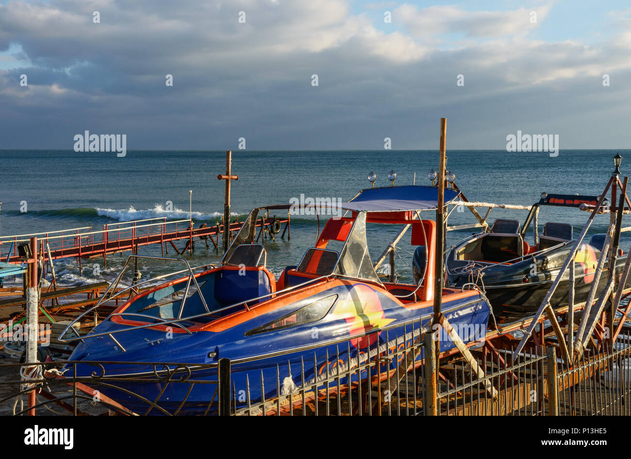 Malerischer Blick auf Motorboote, die auf dem Metall docking Rampe an der Strand flach im Licht des Sonnenuntergangs auf Wasser Hintergrund montiert sind. Stockfoto