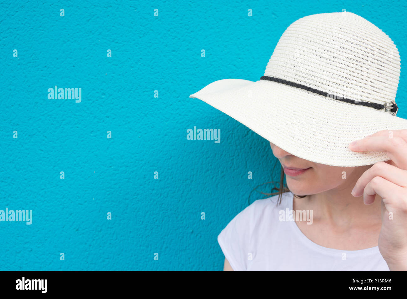 Hübsche Junge kaukasier Frau in Stroh Sonnenhut weißes T-Shirt in türkis gestrichene Wand Hintergrund. Urban Lifestyle Fashion Sommer Wanderlust verbindlich Stockfoto
