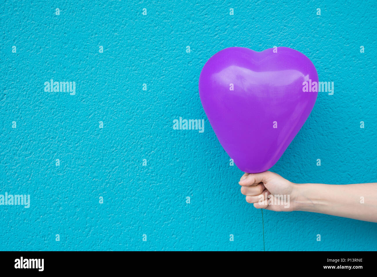 Junge kaukasier Frau Mädchen hält in der Hand Lila Luftballon in Herzform auf türkis gestrichene Wand Hintergrund. Liebe Liebe Spende Kinder gesund Con Stockfoto