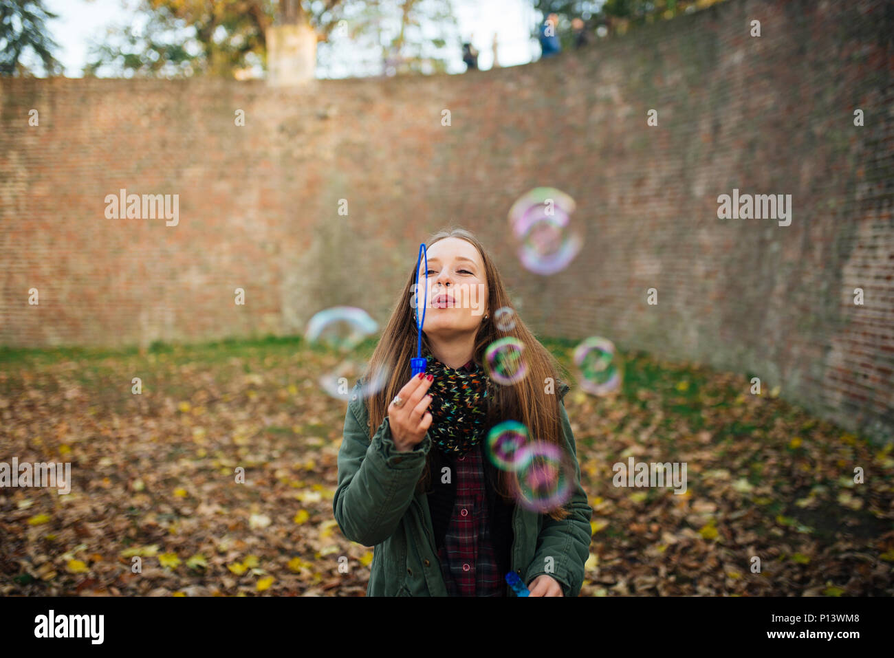 Attraktive junge Frau genießt einen Blasen im öffentlichen Park. Boden bedeckt mit Blätter im Herbst. Stockfoto