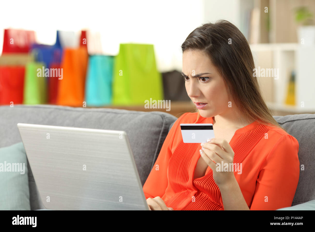 Schockiert Shopper kaufen online mit Kreditkarte auf einer Couch im Wohnzimmer zu Hause sitzen Stockfoto