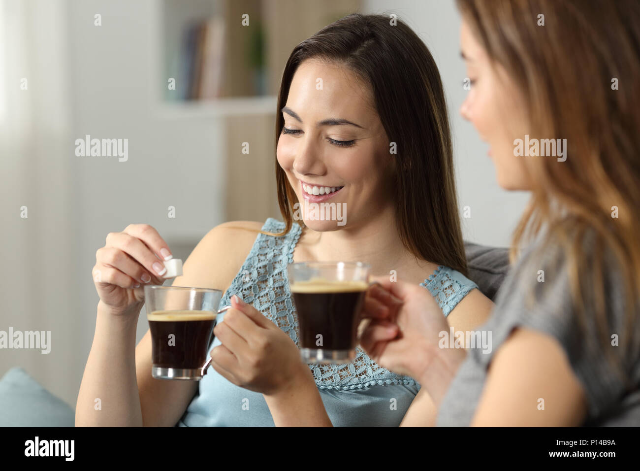 Frauen werfen Würfel Zucker in Kaffee auf einer Couch im Wohnzimmer zu Hause sitzen Stockfoto