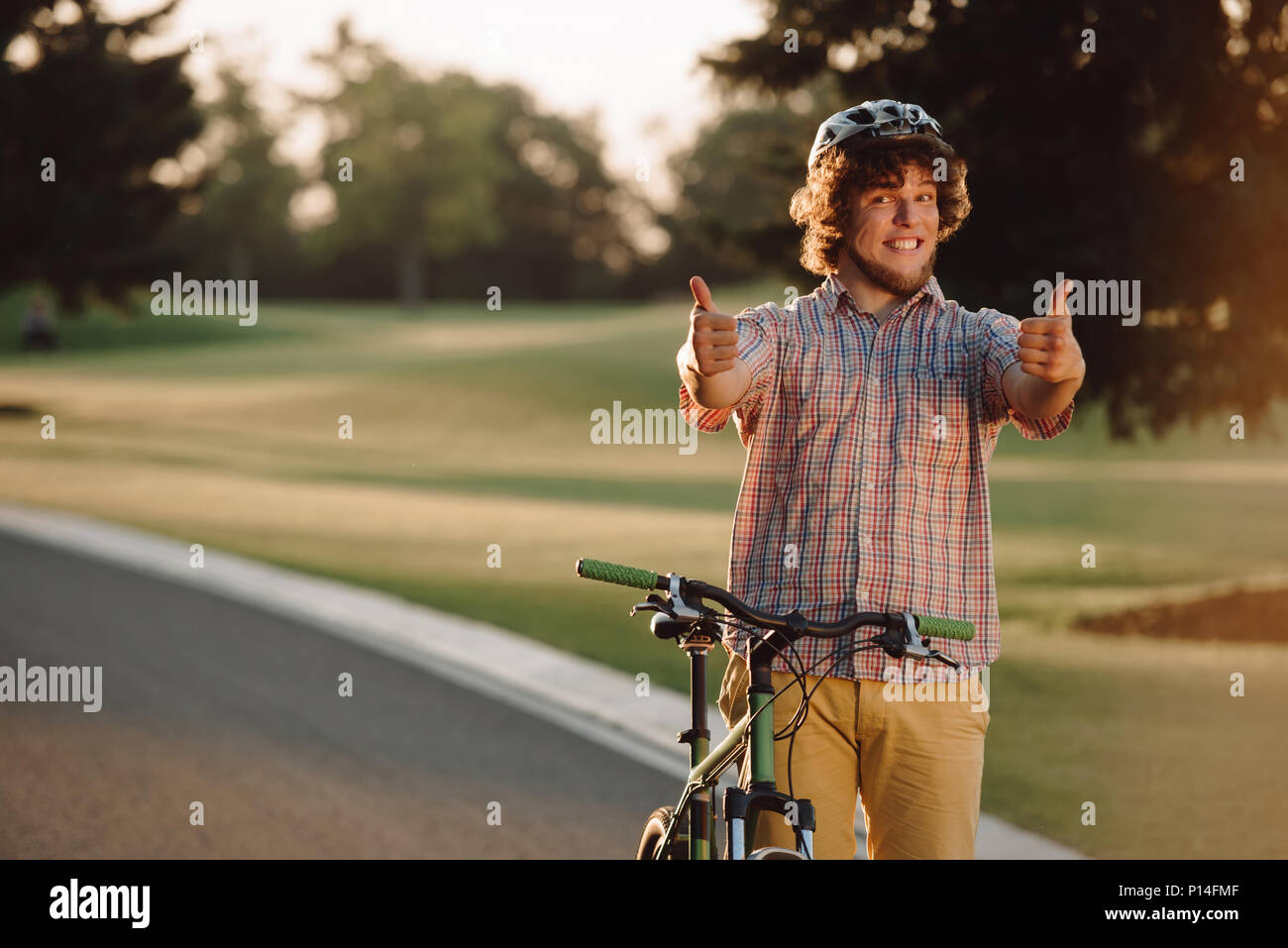 Gerne Radfahrer zwei Daumen hoch im Freien. Portrait von fröhlicher Kerl mit Fahrrad Gestik Daumen nach oben. Aktiv Sommer Freizeitaktivitäten. Genießen Sie Ihr Leben. Stockfoto