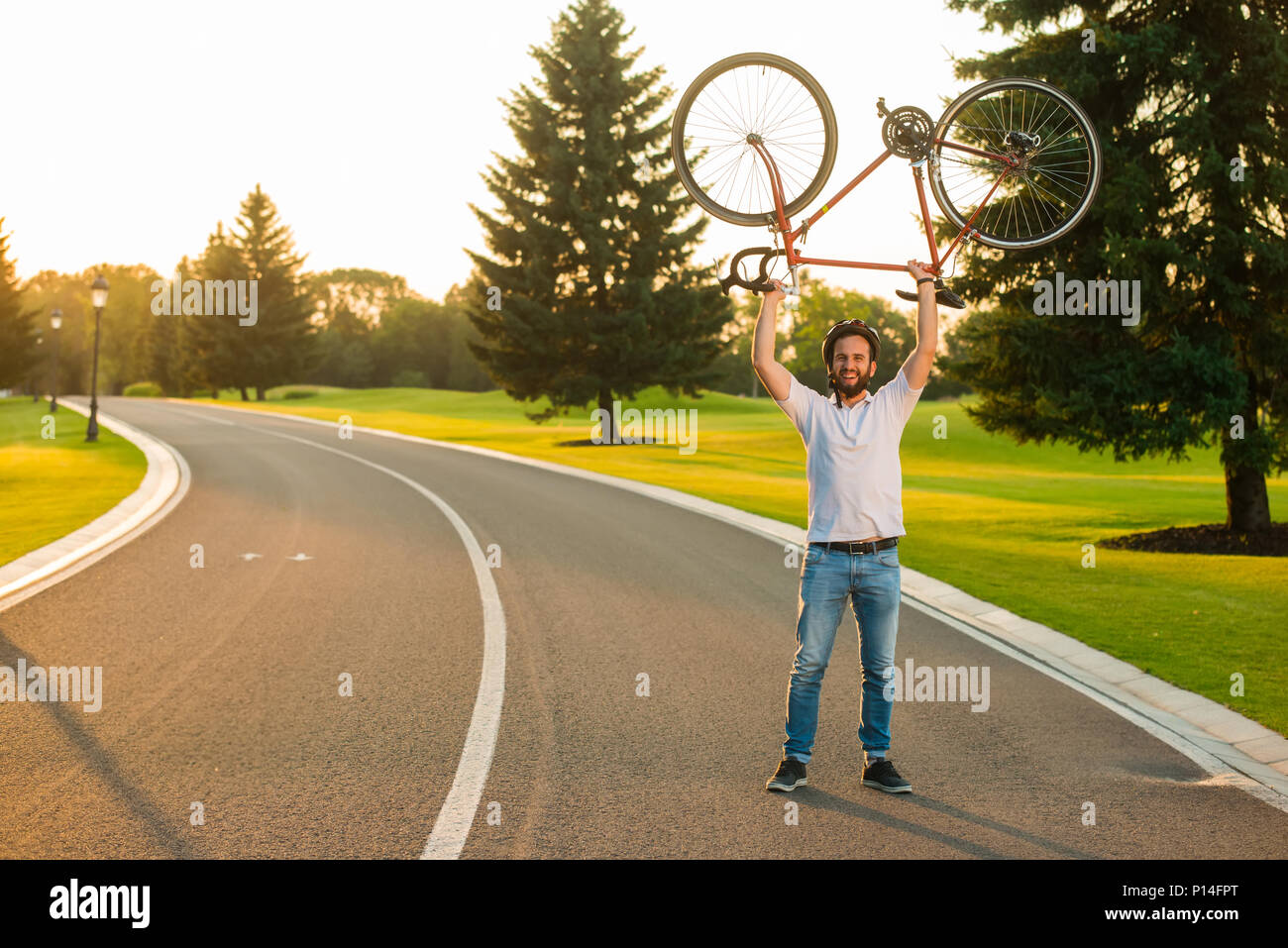 Gerne Radfahrer heben Fahrrad über dem Kopf. Fröhlicher Mensch mit dem Fahrrad auf der Landstraße. Aktiver Lebensstil Konzept. Wie man eine europäische Fahrrad Urlaub nehmen Stockfoto