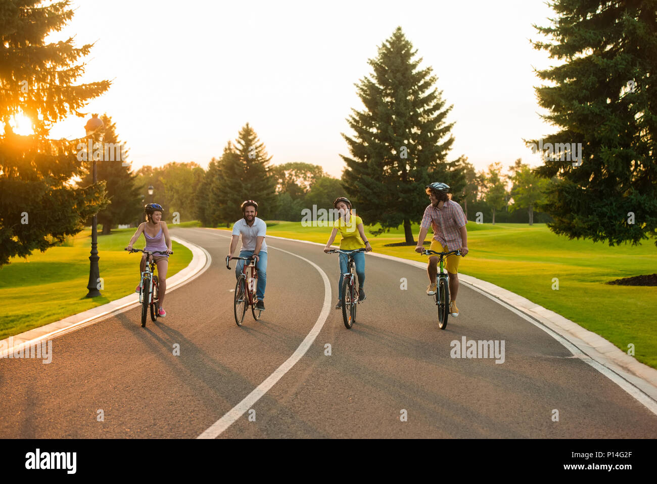 Gruppe von Studenten Radfahren die Straße hinunter. Vier junge Radfahrer reiten auf einer Landstraße, sonnigen Tag. Perfekter Tag für Bike Tour. Stockfoto