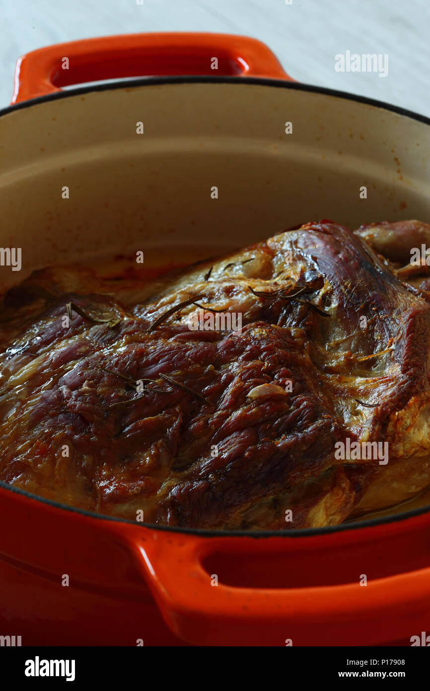 Gebratene Lammschulter in einem orange Keramik braten Teller nach dem Kochen auf Schiefer und grau Holz Küchenarbeitsplatte Stockfoto