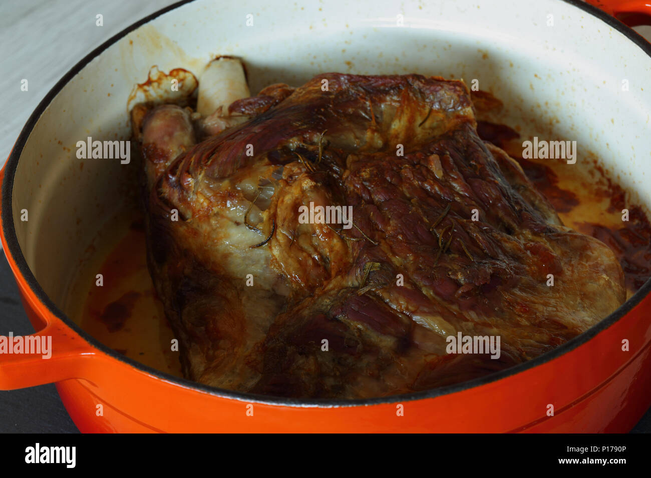 Gebratene Lammschulter in einem orange Keramik braten Teller nach dem Kochen auf Schiefer und grau Holz Küchenarbeitsplatte Stockfoto