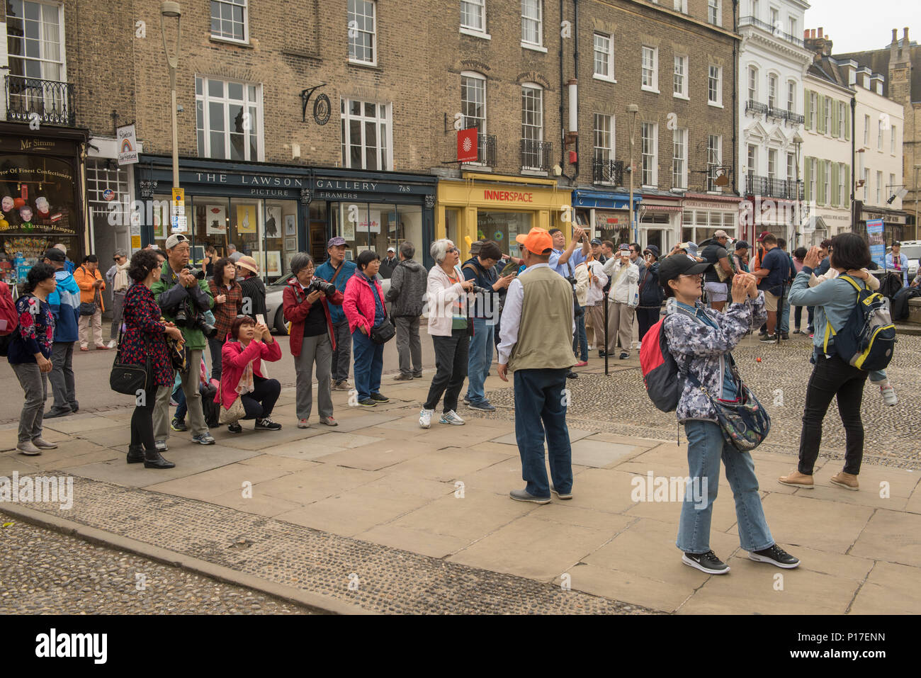Touristen treffen sich auf einer geschäftigen Straße im Zentrum von Cambridge und fotografieren historische Gebäude und Geschäfte an einem bewölkten Tag in diesem beliebten Reiseziel in Großbritannien Stockfoto