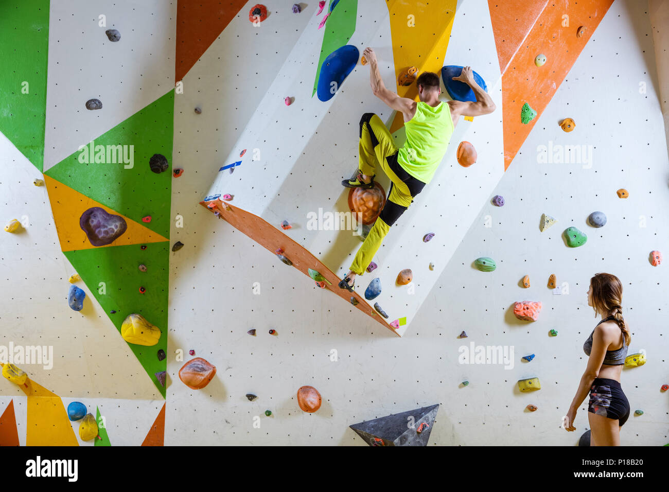 Kletterer in Kletterhalle. Junger Mann klettern Bouldern Problem (Route), Mädchen, Kletterer und ihn beobachtete. Stockfoto